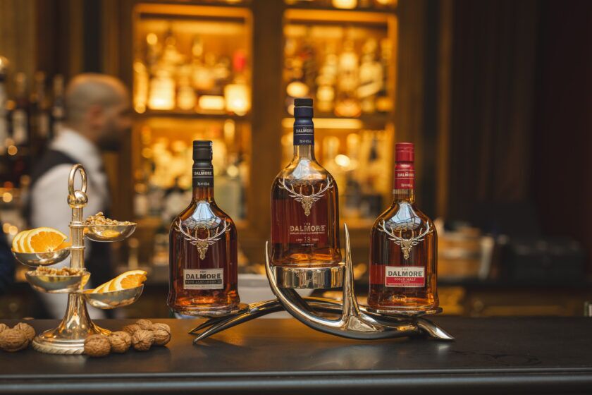 Three Dalmore single malt whisky bottles on a silver antler stand with orange slices and walnuts on a bar, styled scene
