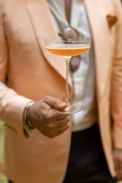 Peach shawl collar dinner jacket with white shirt, worn by a model holding a coupe glass at an event