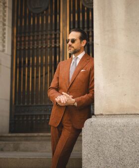 Terracotta textured linen-blend suit with white shirt and grey checked tie, worn by a model on city steps