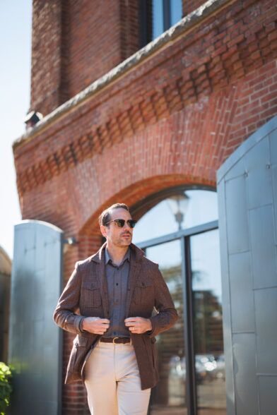 Brown flannel safari jacket over a grey polo with cream trousers, worn by a model