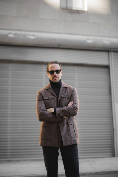 Brown flannel safari jacket over a black turtleneck, worn by a model with arms crossed