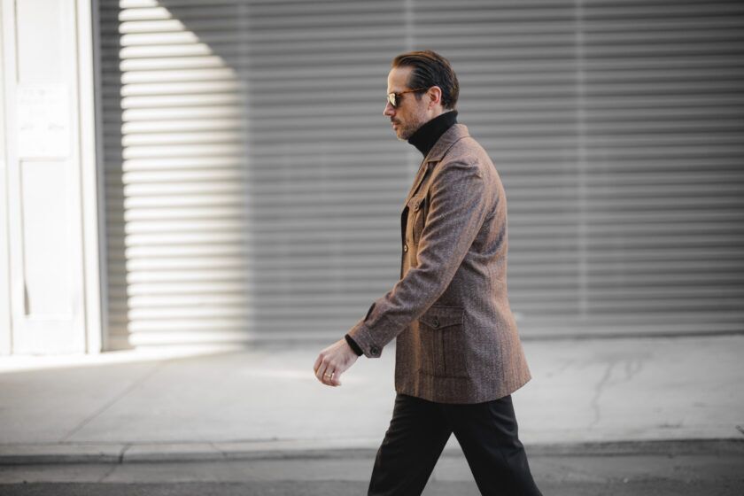 Brown flannel safari jacket over a black turtleneck, worn by a model walking in profile
