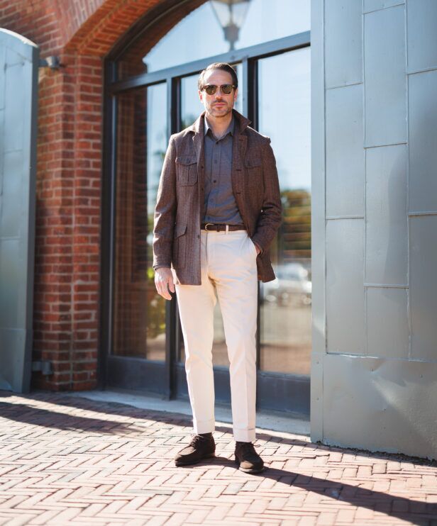 Brown flannel safari jacket with grey polo, cream trousers and suede boots, full length