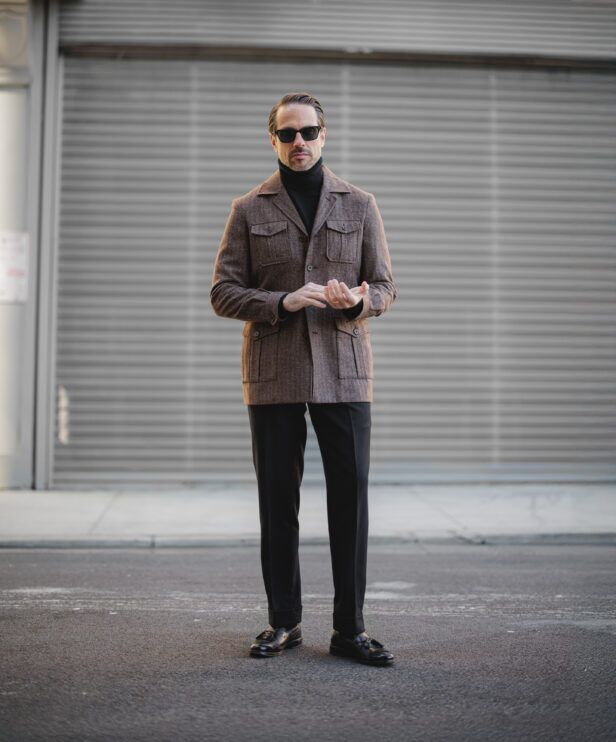 Brown flannel safari jacket with black turtleneck, trousers and tassel loafers, full length
