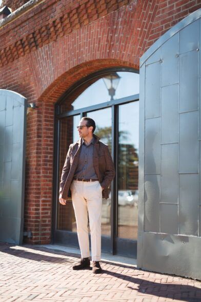 Brown flannel safari jacket over a grey polo with cream trousers, worn by a model