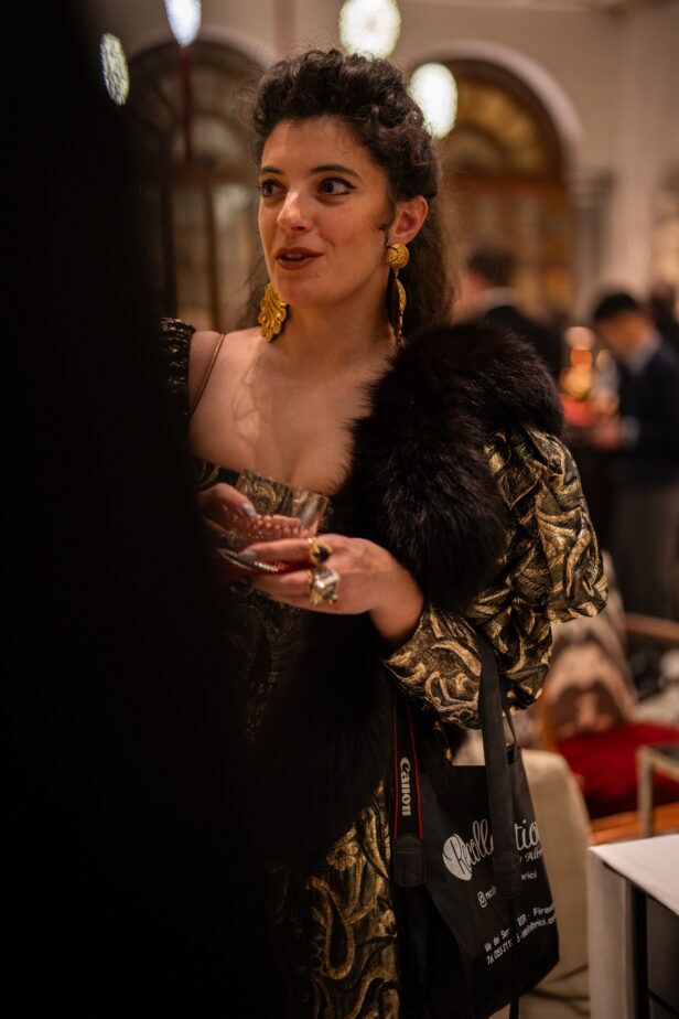 Gold brocade gown with a black fur stole, worn by a guest holding a cocktail