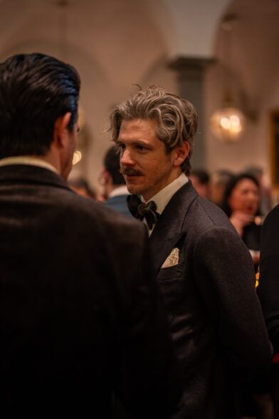 Charcoal flannel jacket with a dark bow tie and cream pocket square, worn by a guest