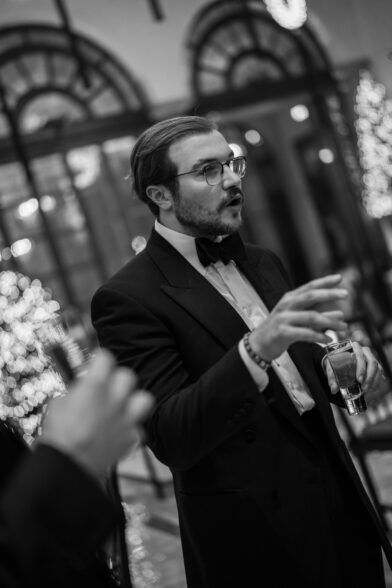 Black peak lapel dinner jacket with bow tie, worn by a guest in a black and white photograph