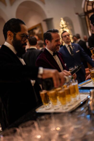 Burgundy velvet dinner jacket with a bow tie, worn by a guest pouring drinks