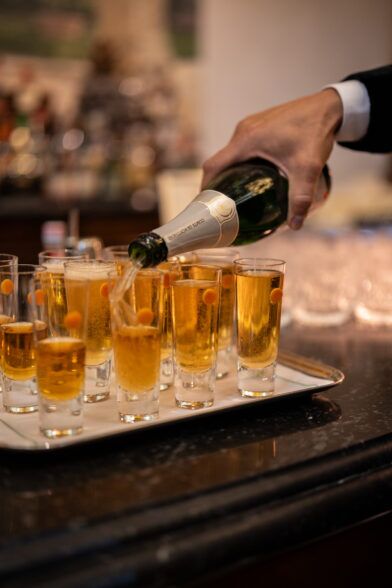 Champagne poured into a tray of flutes at a hotel bar by a guest in black tie