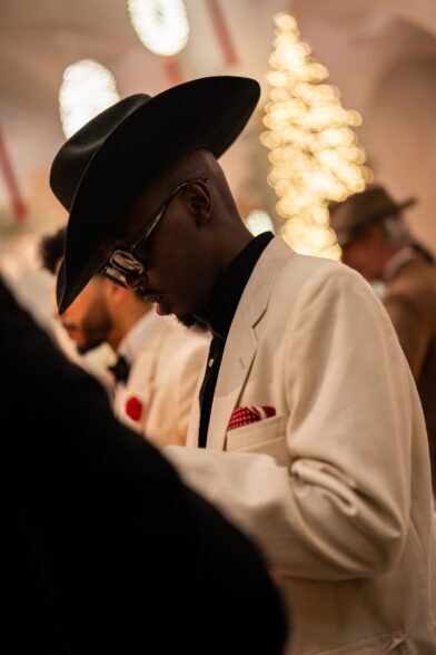 Cream dinner jacket with a black shirt, wide-brimmed hat and red pocket square
