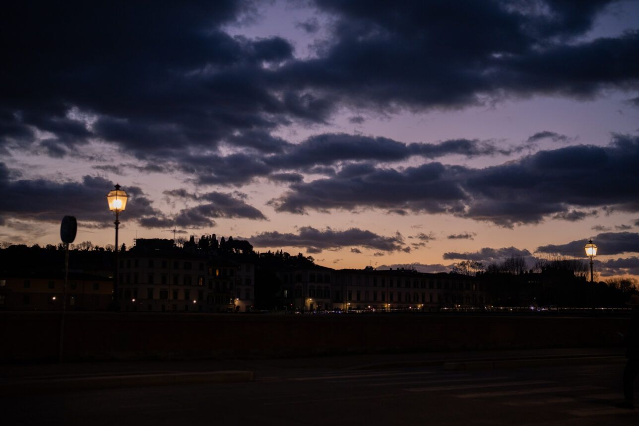 Florence rooftops and street lamps against a violet dusk sky beside the Arno