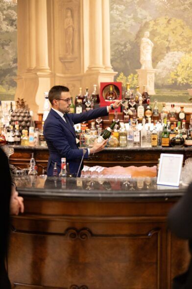 Navy suit with a patterned tie, worn by a bartender pouring champagne at a hotel bar