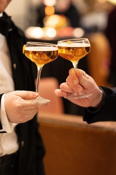Two coupe glasses of champagne raised in a toast by guests in black tie