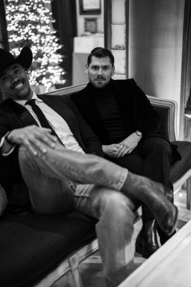 Black velvet jacket over a turtleneck, worn by a seated guest beside a hat and jeans