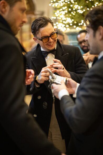 Black overcoat over a bow tie and dinner jacket, worn by a guest at a lit evening party