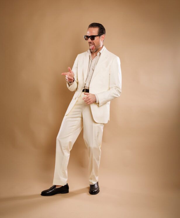 Ivory twill suit with stone shirt and brown loafers, worn by a model, full length