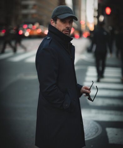 Dark twill storm coat with a stand collar and flat cap, worn by a model at a city crossing