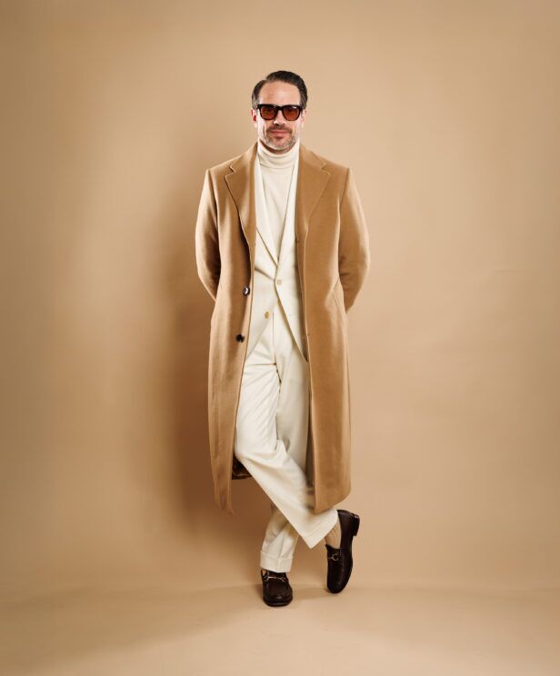Camel overcoat over ivory flannel suit with cream turtleneck and brown bit loafers, worn by a model