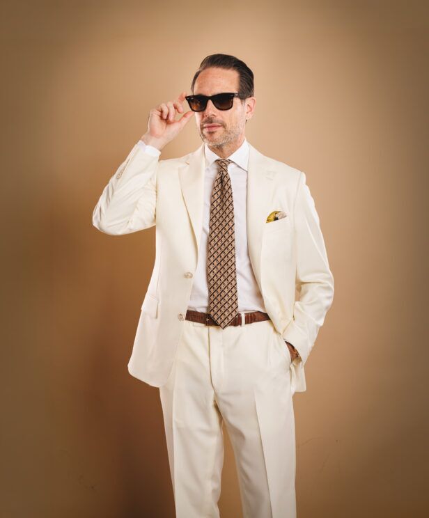 Ivory two-button suit with white shirt, brown geometric silk necktie and gold pocket square, worn by a model