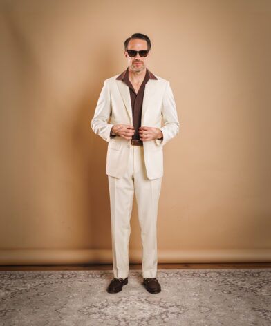 Ivory two-piece suit with brown knit polo and brown bit loafers, worn by a model