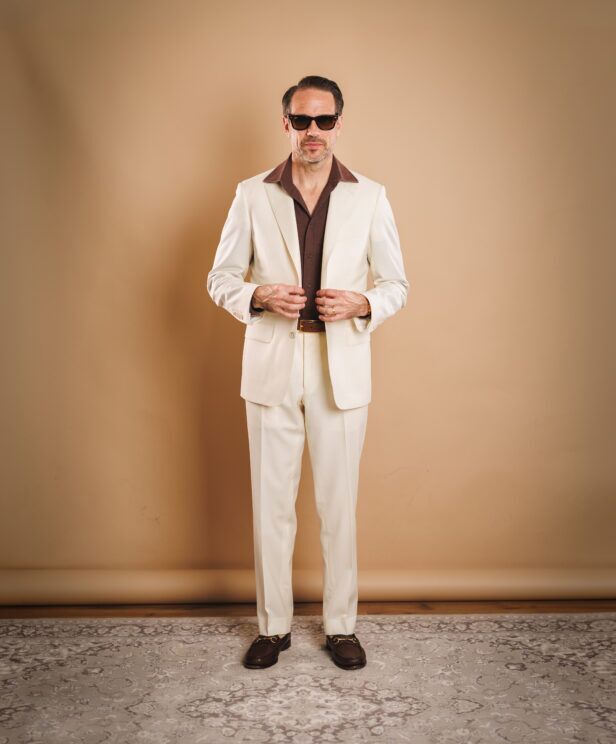 Ivory two-piece suit with brown knit polo and brown bit loafers, worn by a model