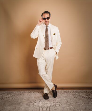 Ivory two-button suit with white shirt, brown geometric silk tie and brown bit loafers, worn by a model