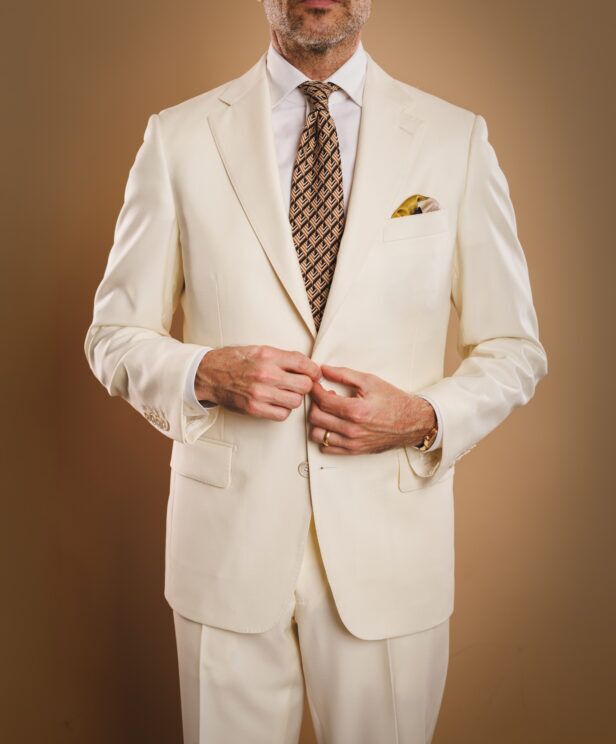 Ivory single-breasted suit with white shirt, tan geometric silk tie and gold pocket square, worn by a model