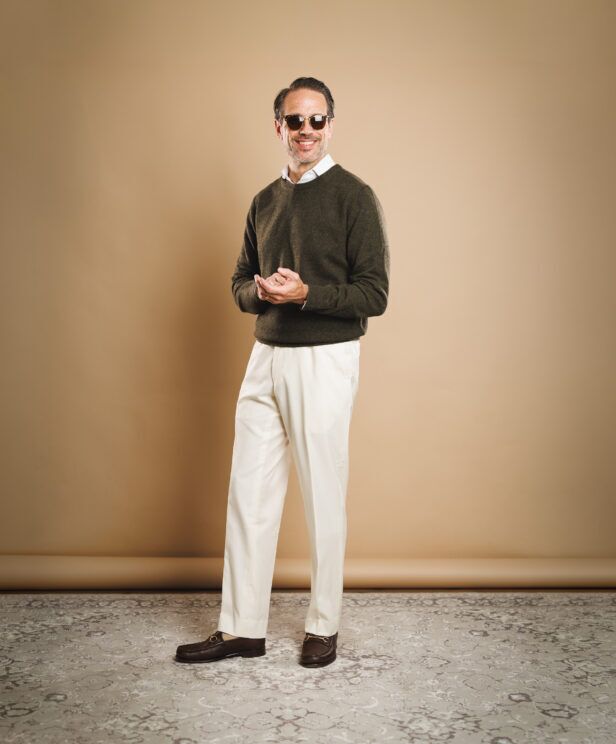 Olive crewneck sweater with white shirt, cream pleated trousers and brown bit loafers, worn by a model
