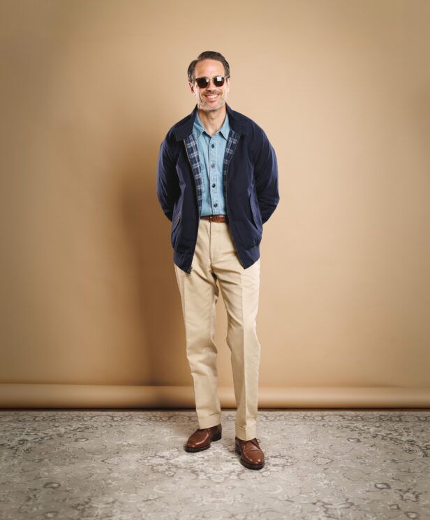 Navy Harrington jacket with plaid lining, chambray shirt, khaki trousers and brown derbies, worn by a model