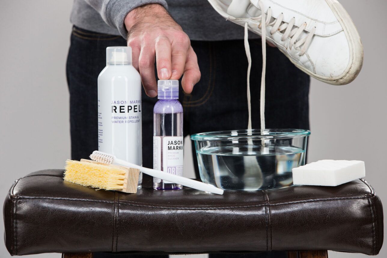 Sneaker cleaning kit with repellent spray, cleaner, brushes and sponge beside a white leather sneaker