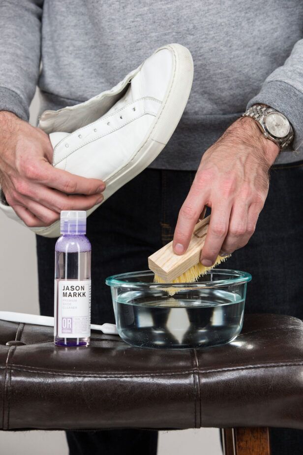 Premium shoe cleaner bottle and wooden brush dipped in water beside a white leather sneaker, a styled cleaning scene