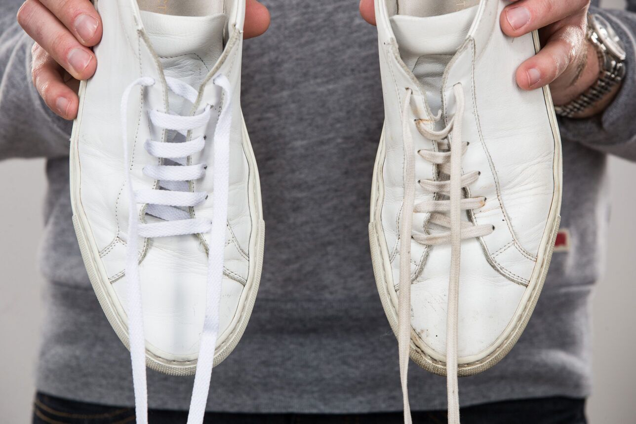 White leather sneakers held side by side, one with fresh laces and one scuffed, a close-up detail