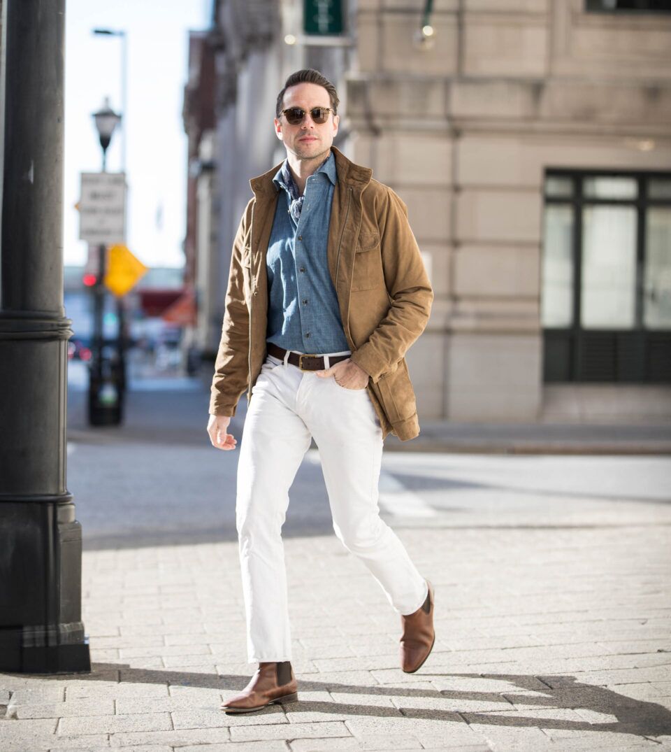 Tan suede field jacket with chambray shirt, white jeans and brown Chelsea boots, worn by a model on a city street