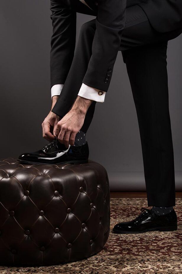 Black tuxedo trousers with satin side stripe and black patent oxfords, worn by a model lacing a shoe