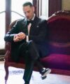 Black peak lapel tuxedo with black bow tie, white shirt and pocket square, worn by a model on a velvet settee