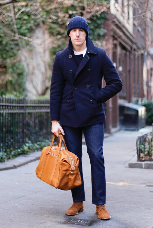 Navy wool double-breasted peacoat with ribbed watch cap, dark denim, tan leather weekender and suede boots, worn by a model on a city street
