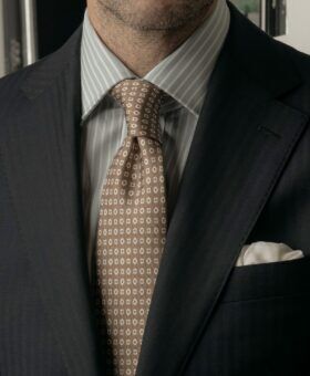 Navy herringbone suit jacket with blue striped shirt, tan medallion silk tie and white pocket square, worn by a model