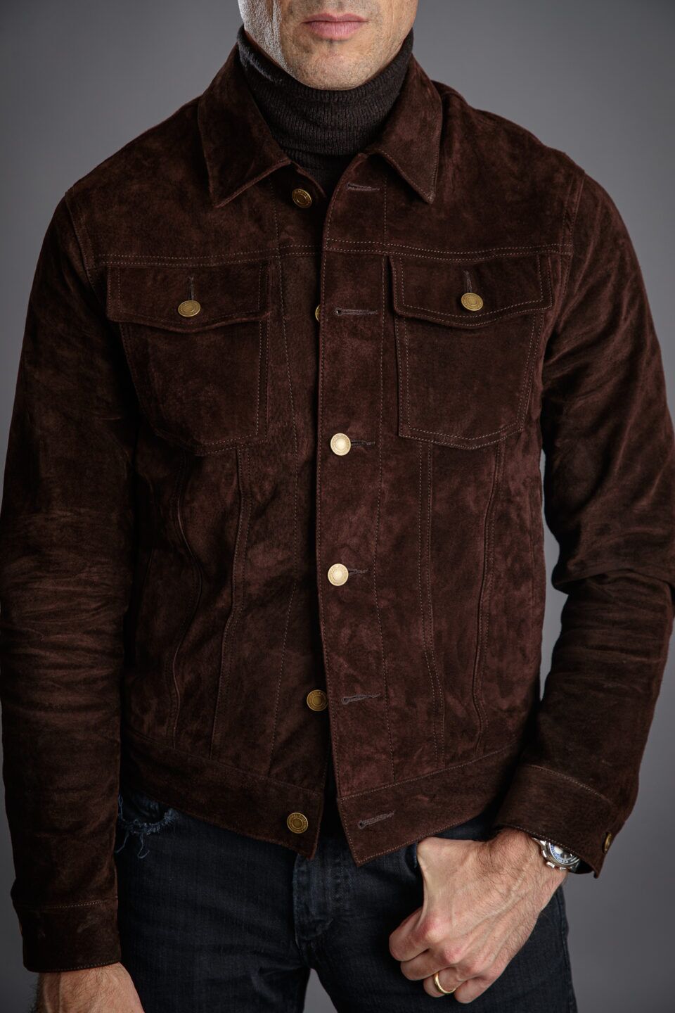 Brown suede trucker jacket with brass buttons, brown turtleneck and dark jeans, worn by a model