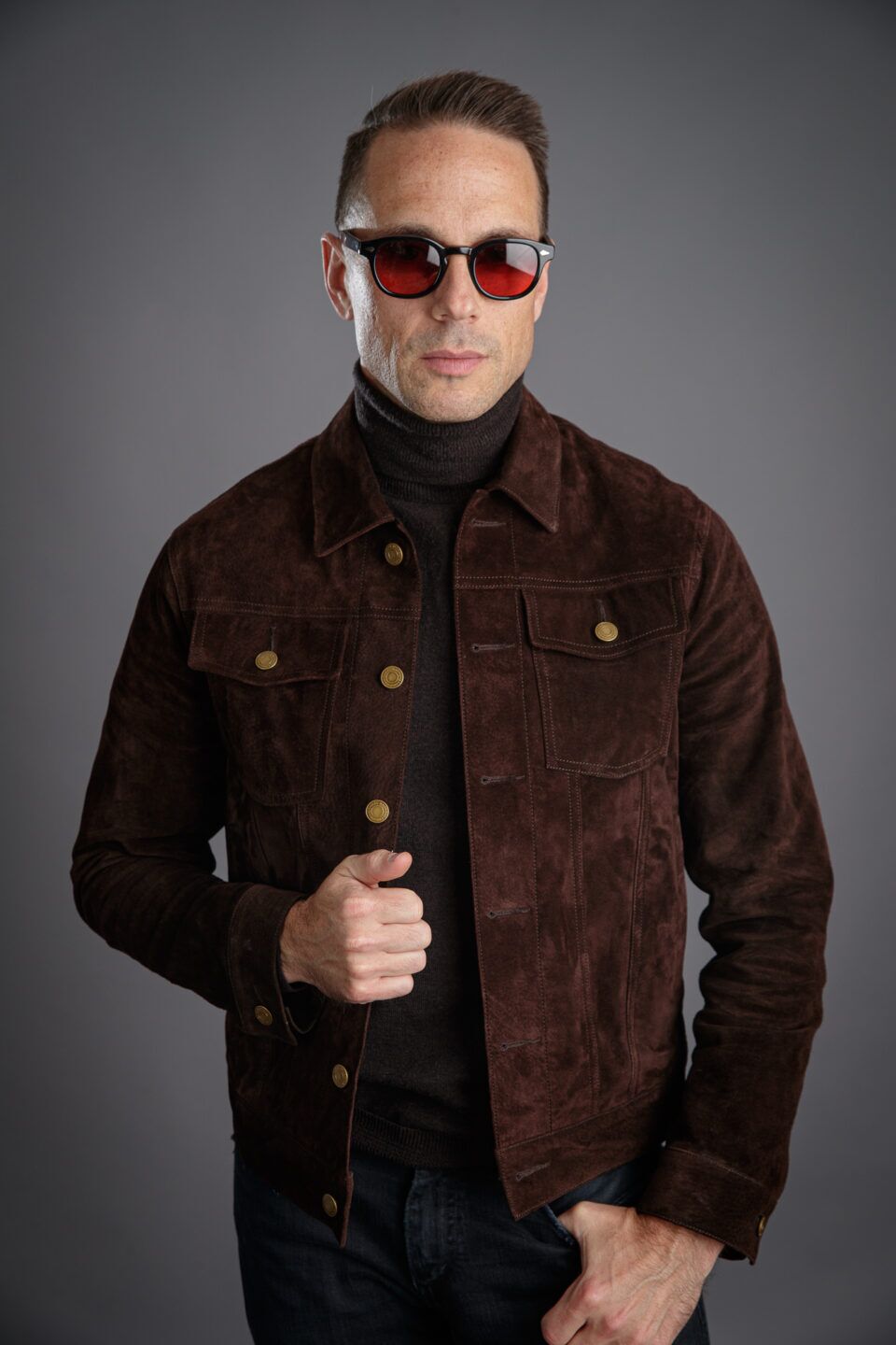 Brown suede trucker jacket with brass buttons, worn over a dark turtleneck and jeans by a model