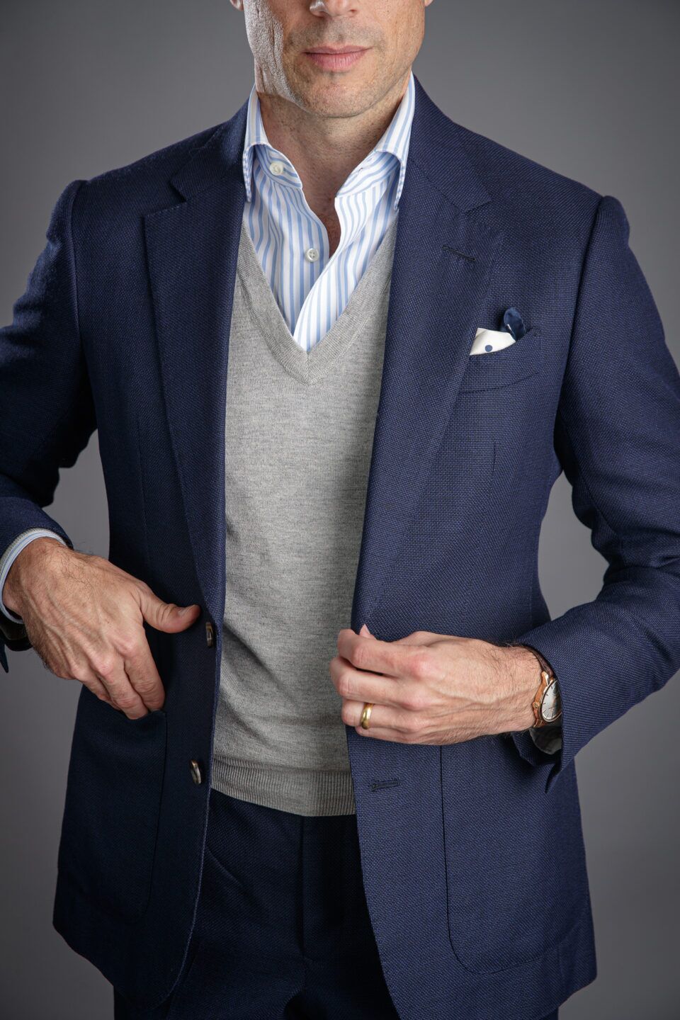 Grey wool V-neck sweater with navy hopsack blazer, blue striped shirt and dotted pocket square, worn by a model