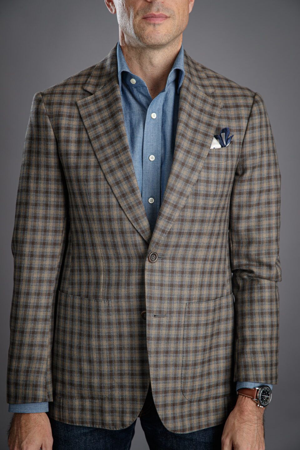 Tan and brown gun club check sport coat with chambray shirt and navy pocket square, worn by a model