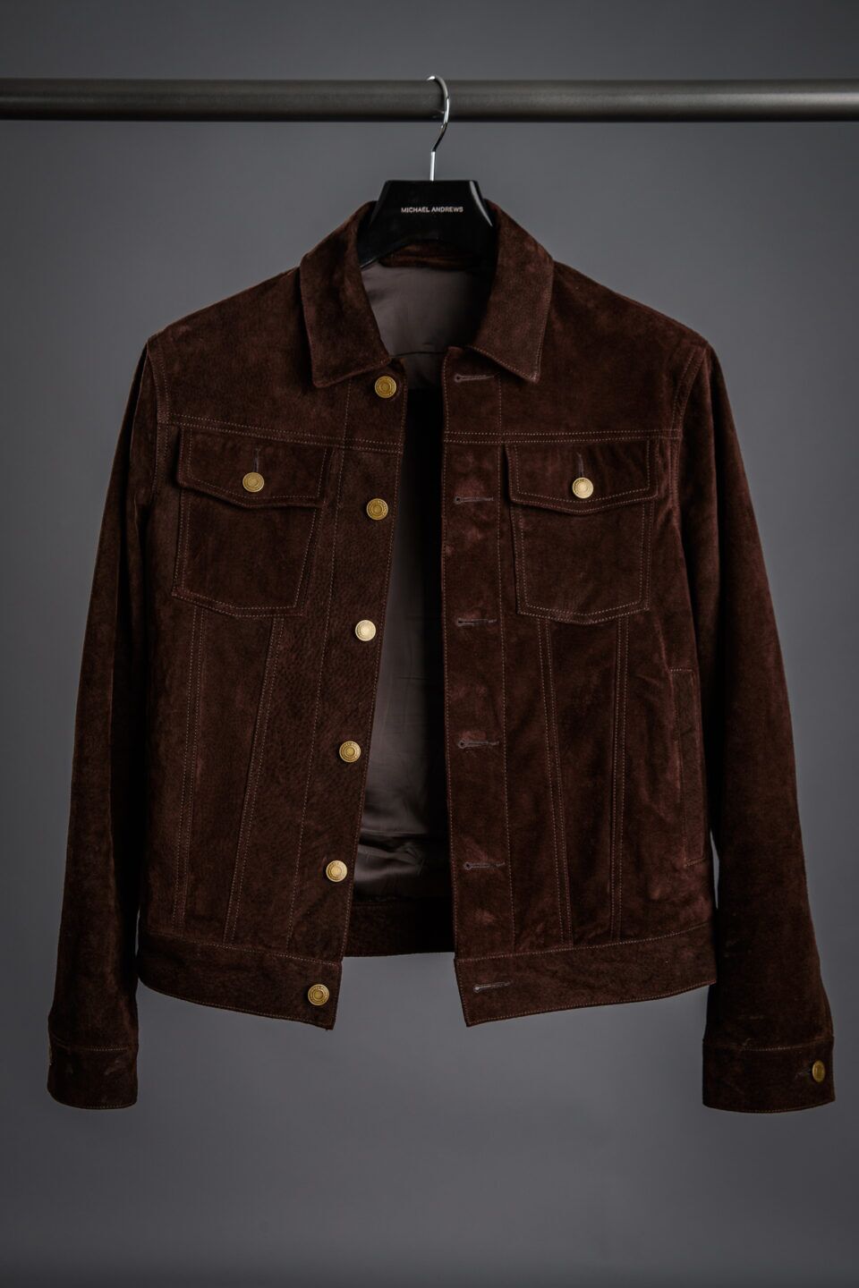 Brown suede trucker jacket with brass buttons, chest pockets and contrast stitching, shown on a hanger