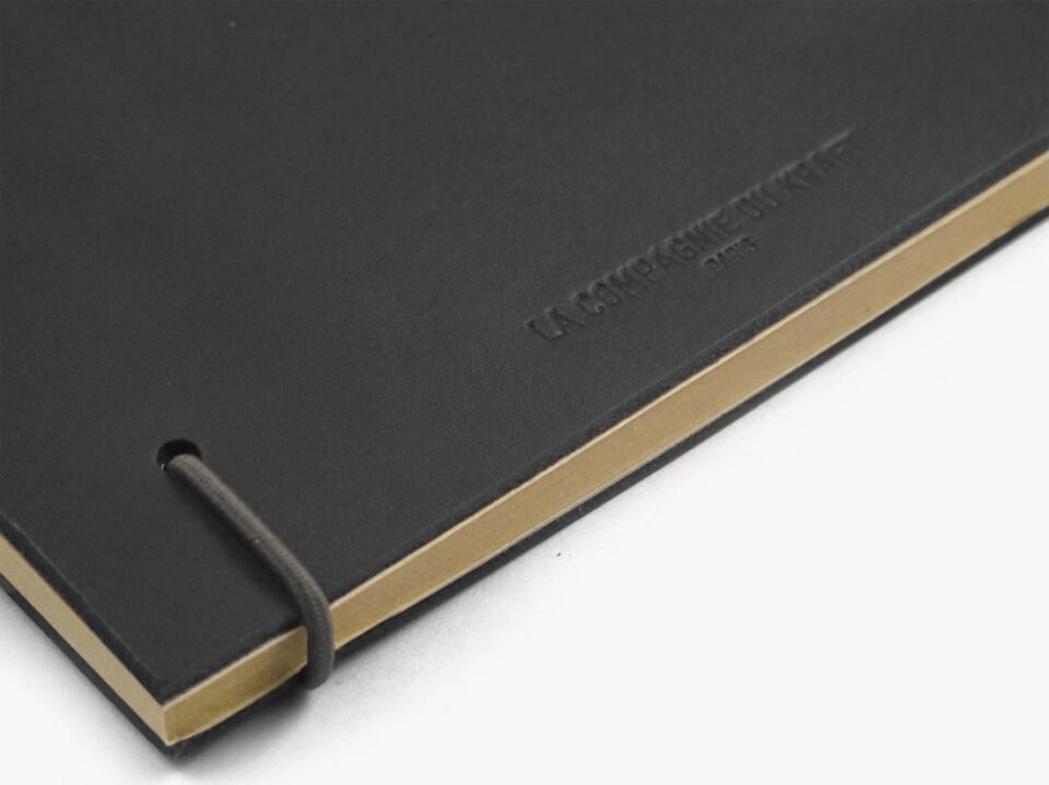 Black leather notebook with embossed logo, elastic closure and kraft pages, a close-up detail