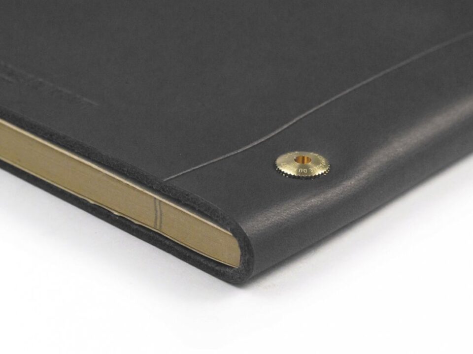 Black leather notebook cover with brass screw post and cream pages, a close-up of the corner