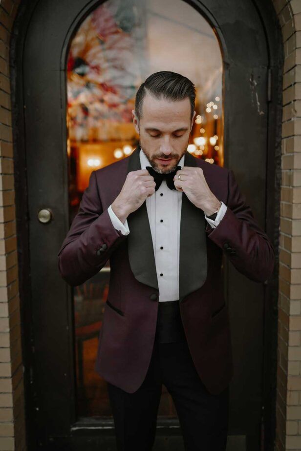Burgundy shawl collar dinner jacket with black bow tie and pleated shirt, worn in a doorway