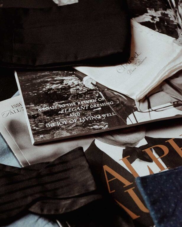 Black silk cummerbund and bow tie with white pocket square and magazines, styled flat lay