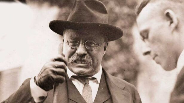 Felt fedora, round wire-rim spectacles and dark suit with textured tie, worn by Theodore Roosevelt in a vintage photo