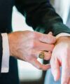 Black dinner jacket sleeve with white shirt cuff and gold monogram signet ring, a close-up detail