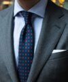 Navy silk necktie with red and blue medallions, worn with a grey flannel suit, a close-up